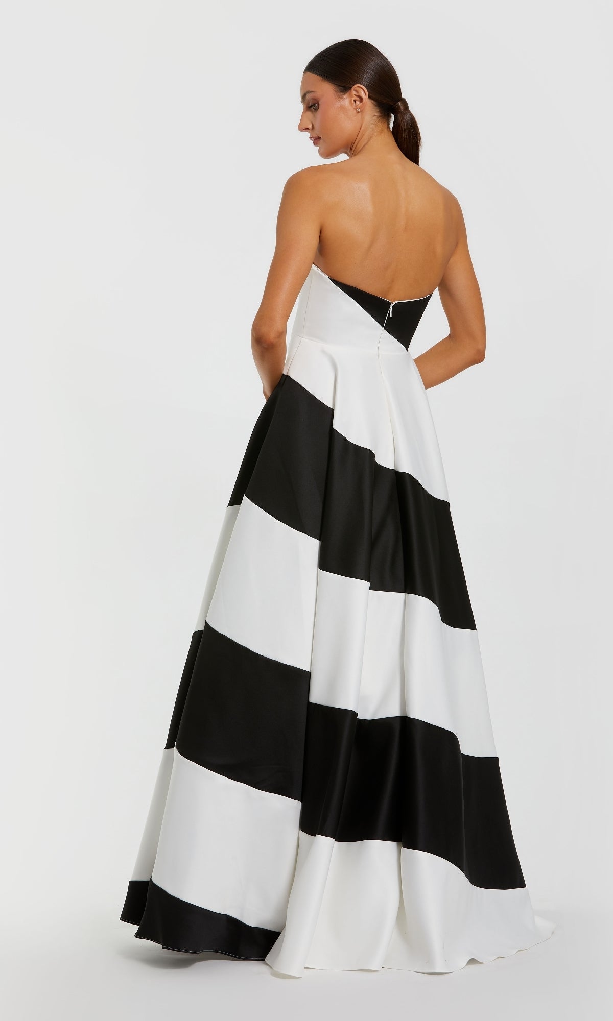 A woman stands facing away in the Mac Duggal 56190 black and white long formal gown, featuring wide horizontal stripes, a strapless neckline, and an elegant A-line silhouette.